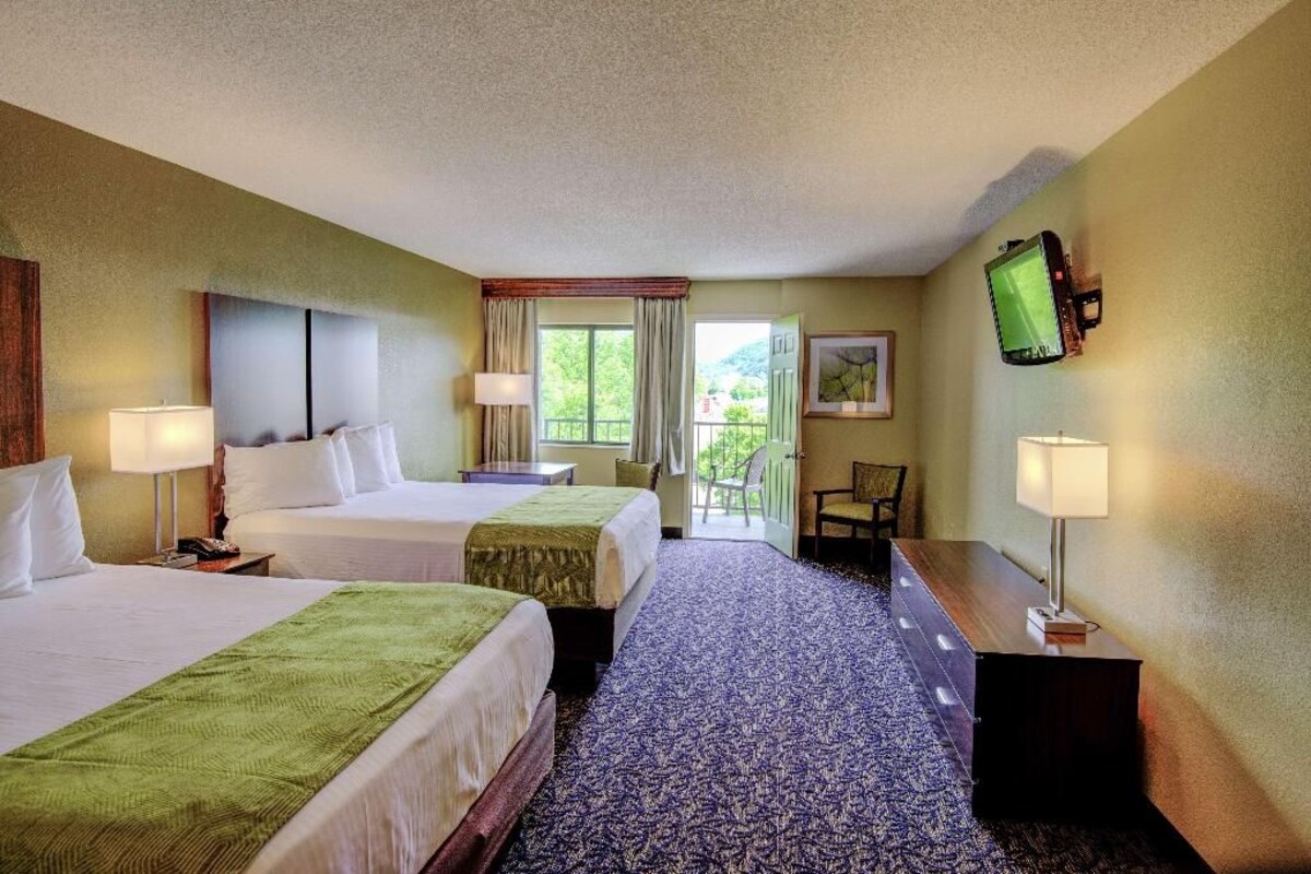 A hotel room with two beds, a desk, a chair, a television, and a window with curtains.