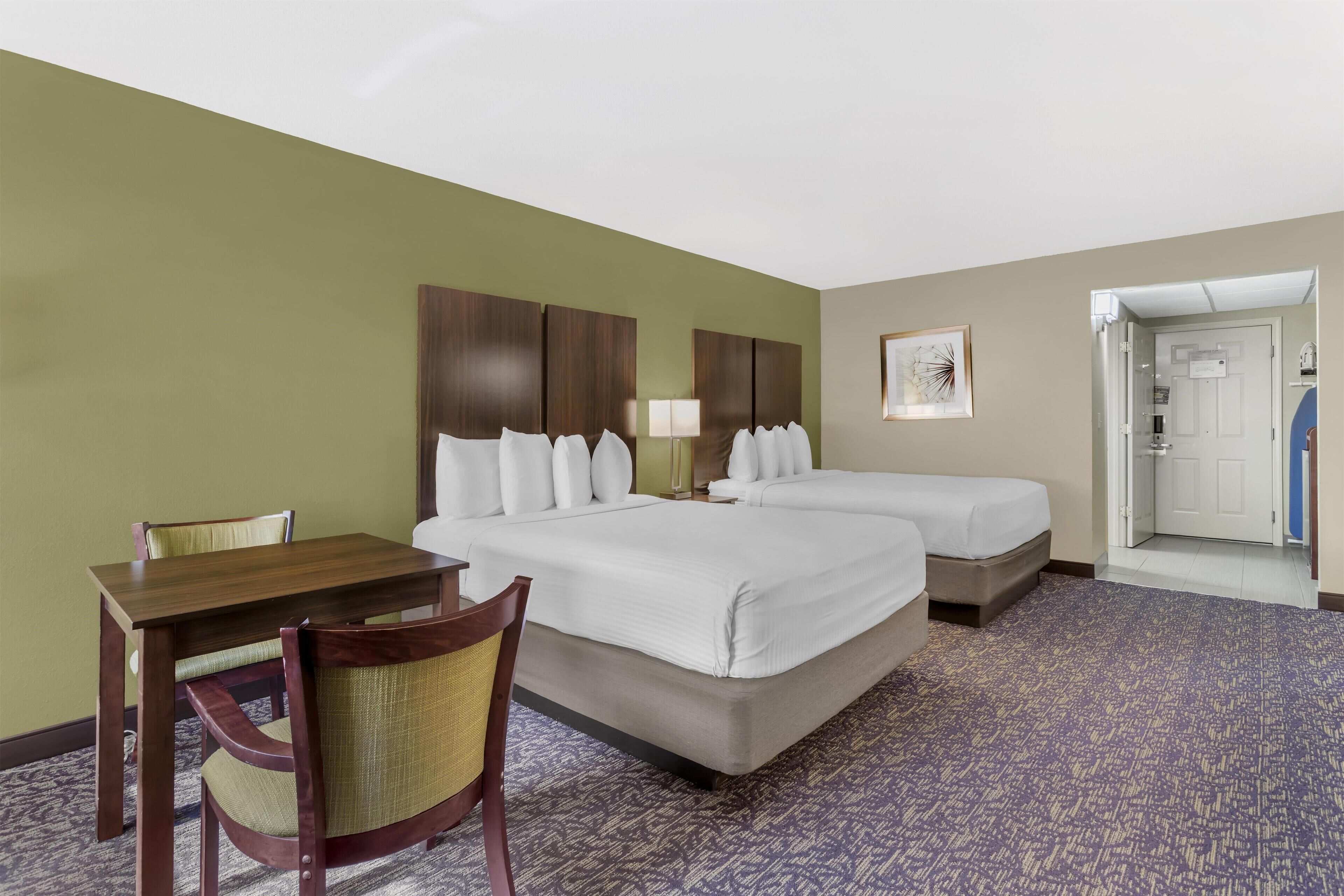 A hotel room with two beds, a desk, a chair, and a carpeted floor.