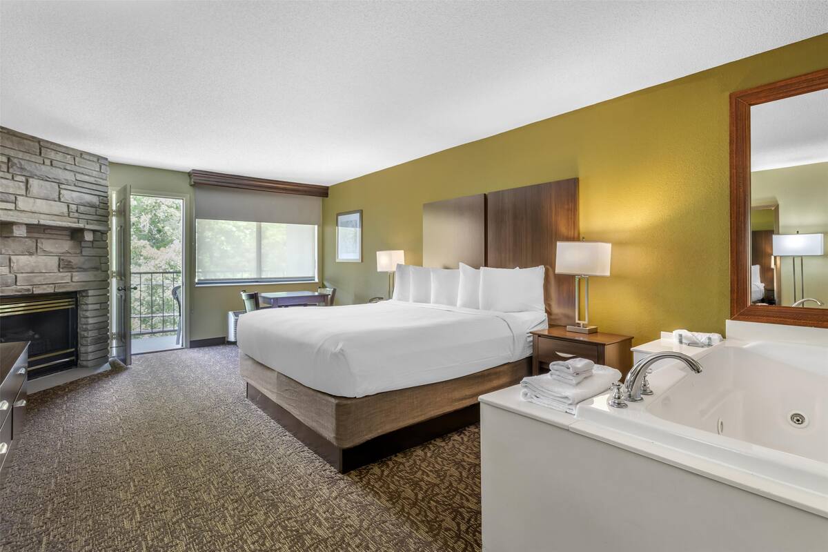 Une chambre d’hôtel avec un grand lit, une salle de bain avec baignoire, une cheminée et une vue sur l’extérieur.