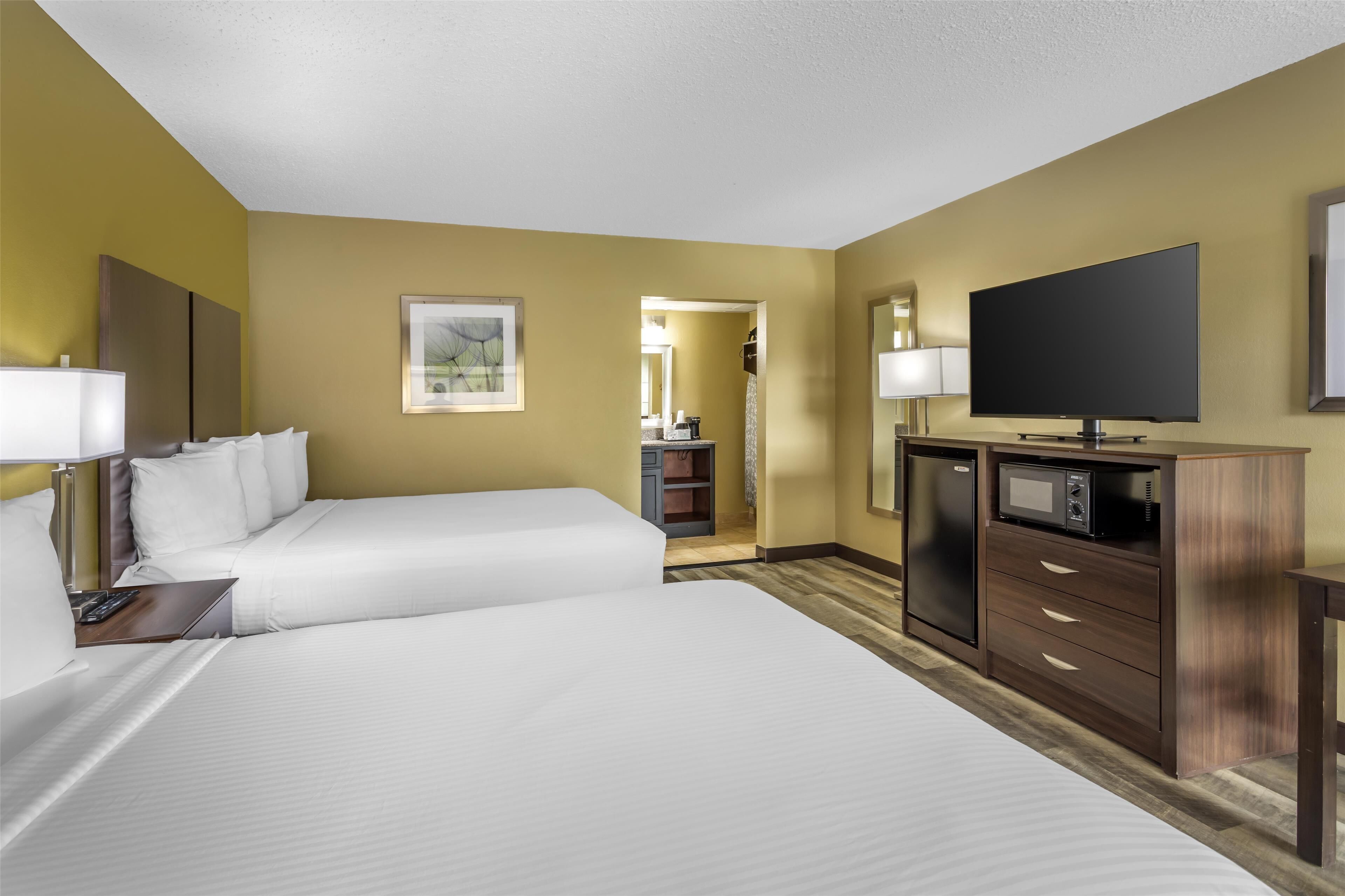 A hotel room with two beds, a TV, a desk with a lamp, and a microwave.