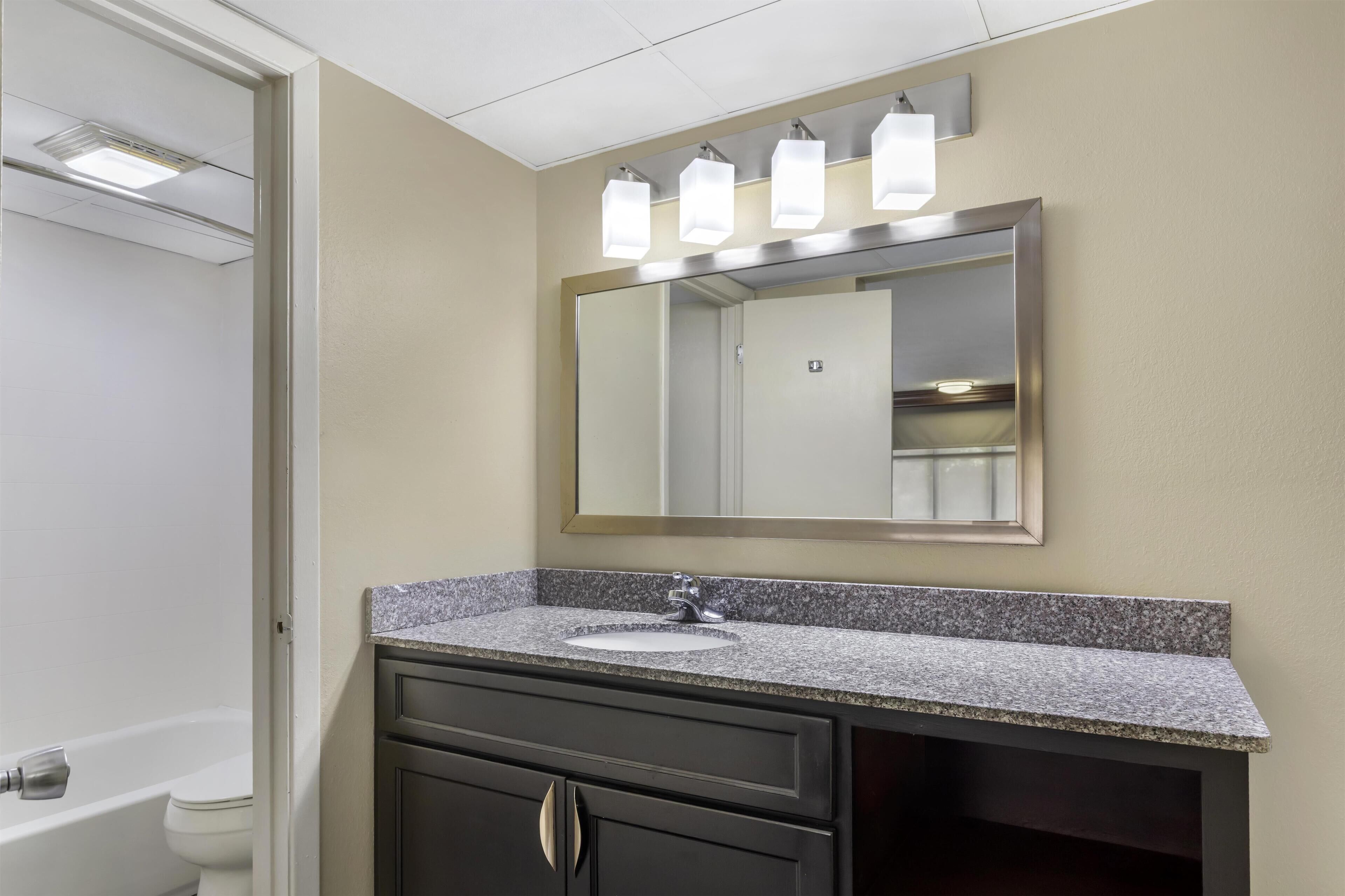 A bathroom with a granite countertop, a sink, a mirror, and a toilet.