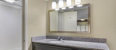 A bathroom with a granite countertop, a sink, a mirror, and a toilet.