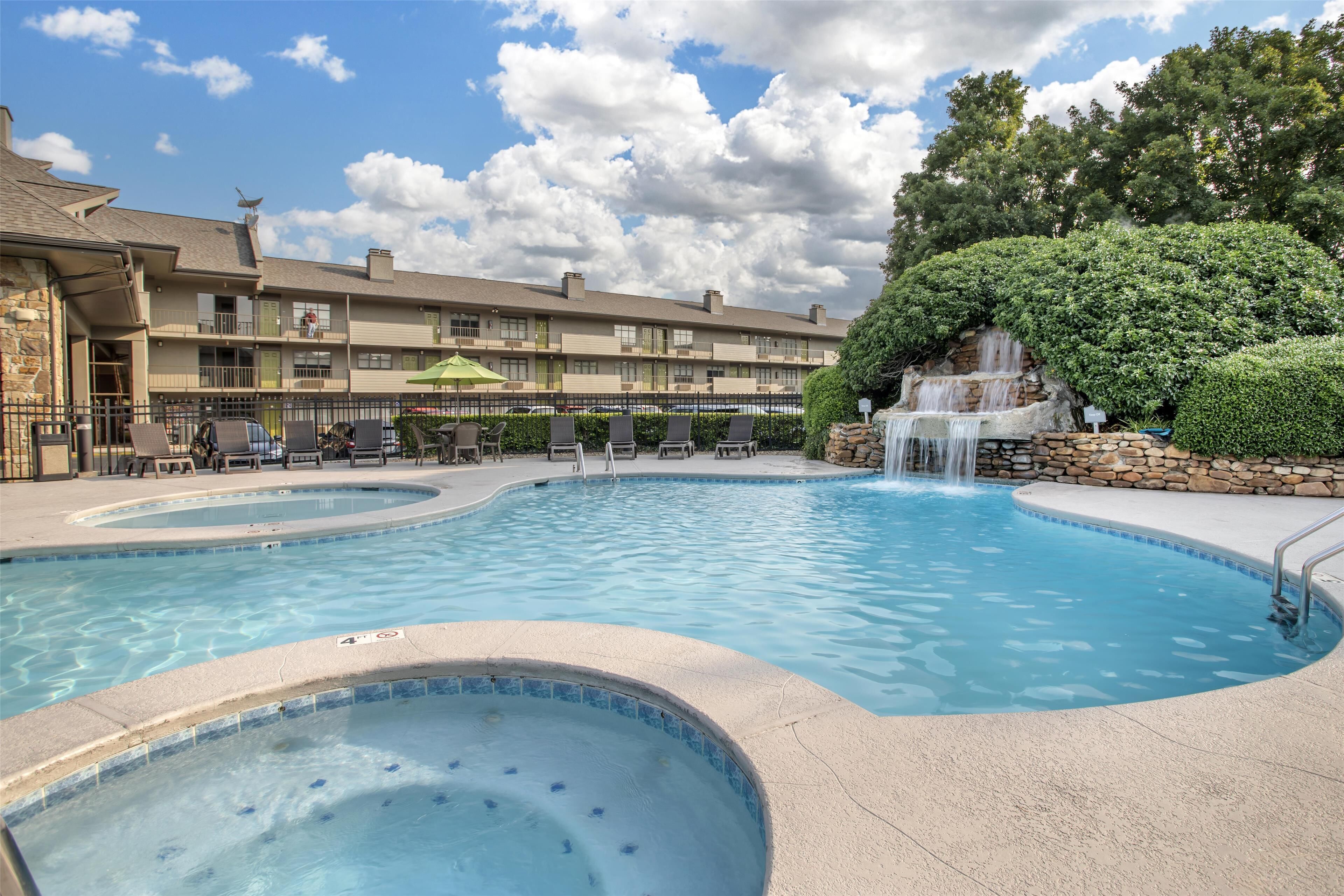 A hotel with a swimming pool, lounge chairs, and a waterfall feature.