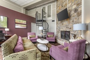 A living room with a stone fireplace, a spiral staircase, and a flat-screen TV mounted on the wall.