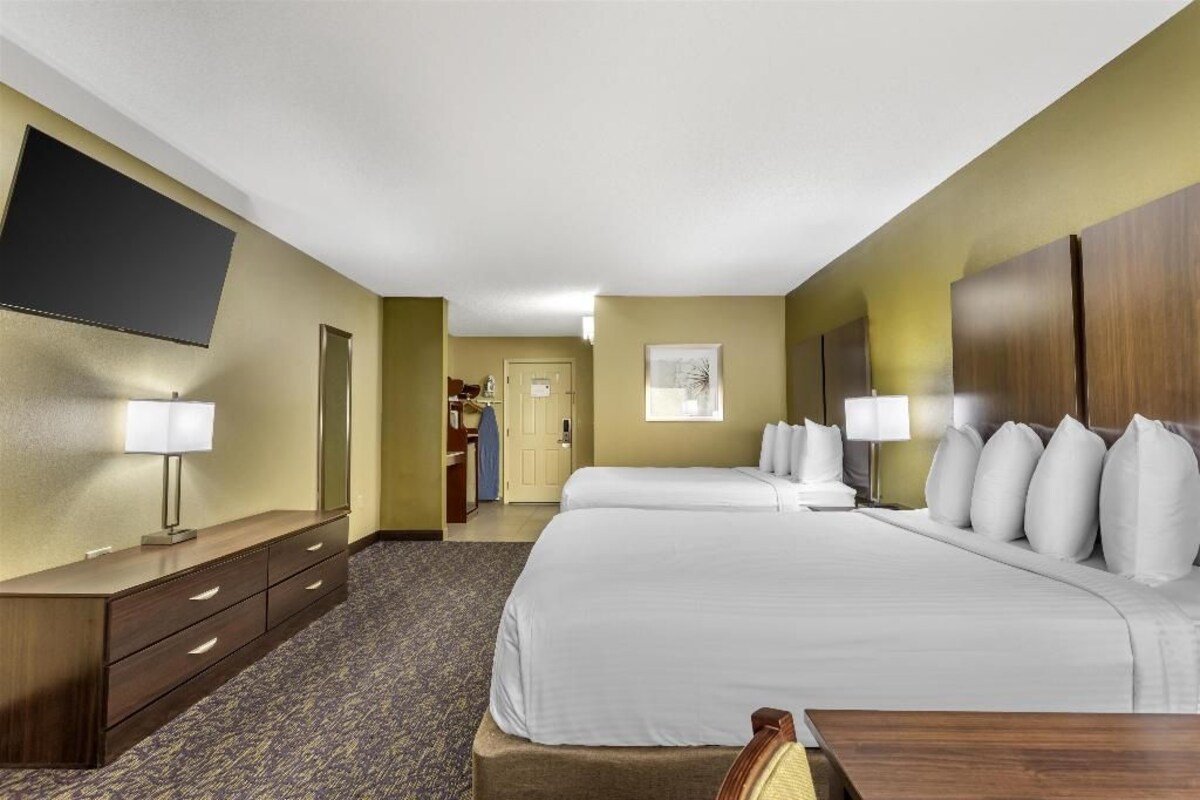 A hotel room with two beds, a flat-screen TV mounted on the wall, a desk with drawers, and a carpeted floor.