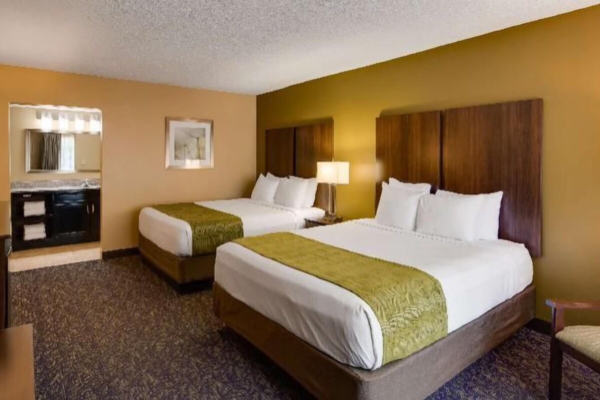 A hotel room with two beds, a desk, a television, and a mirror.