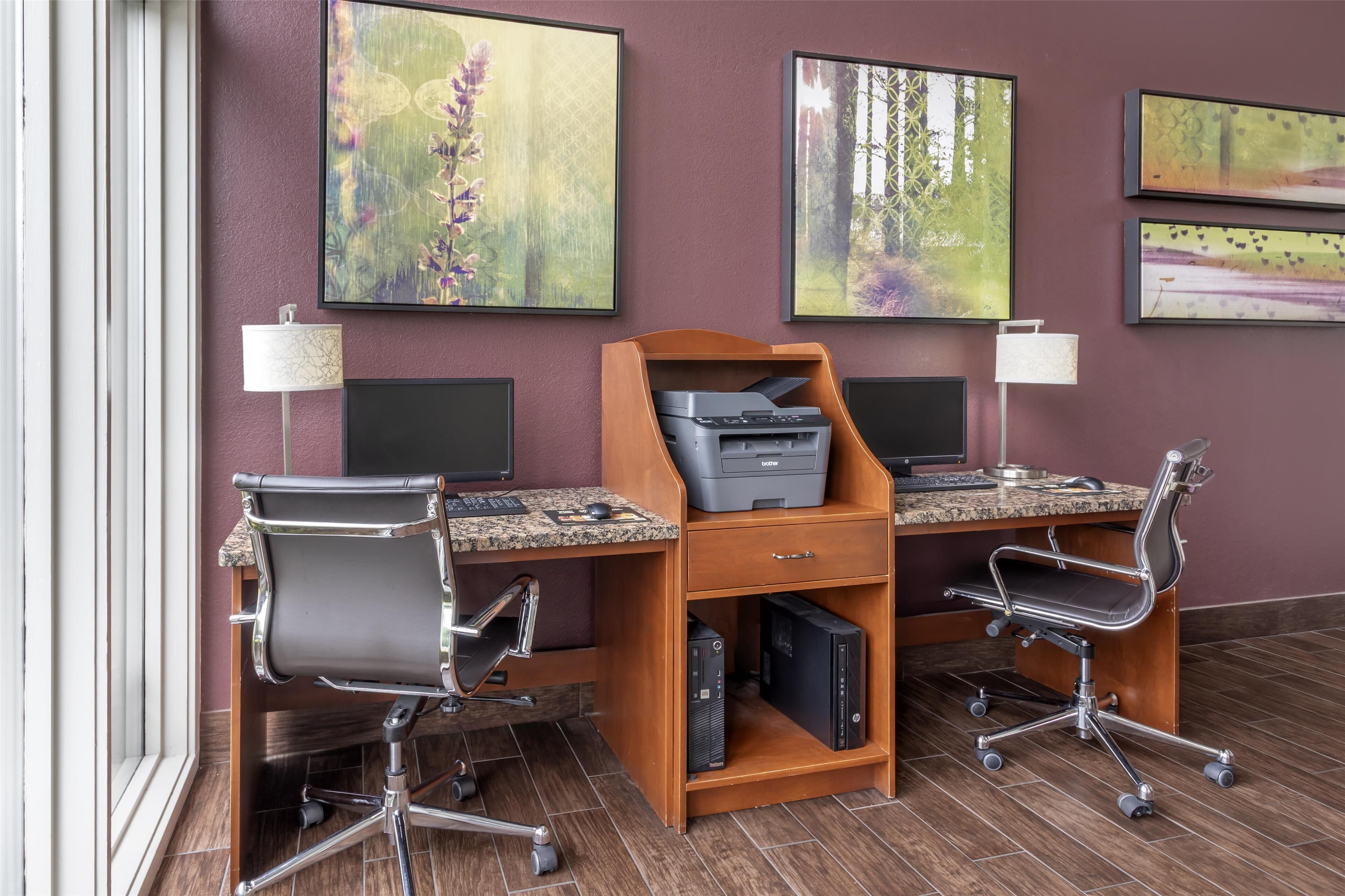 A workspace with two desks, each with a computer and a printer, ergonomic chairs, and framed artwork on the wall.