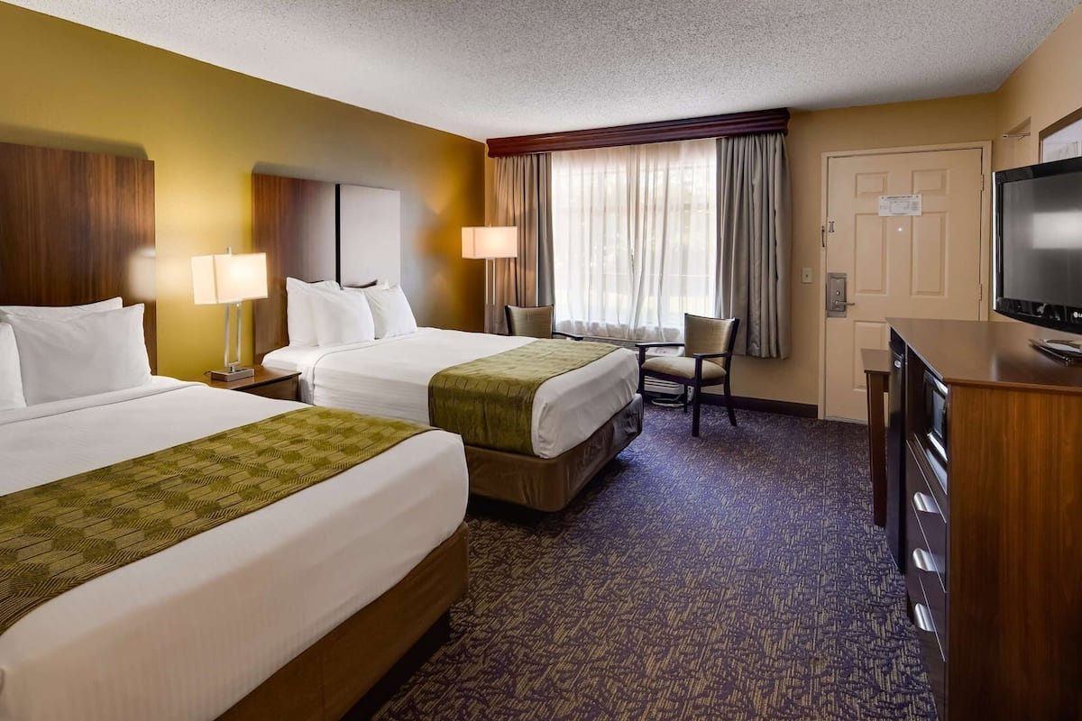 A hotel room with two beds, a desk, a television, and a chair.