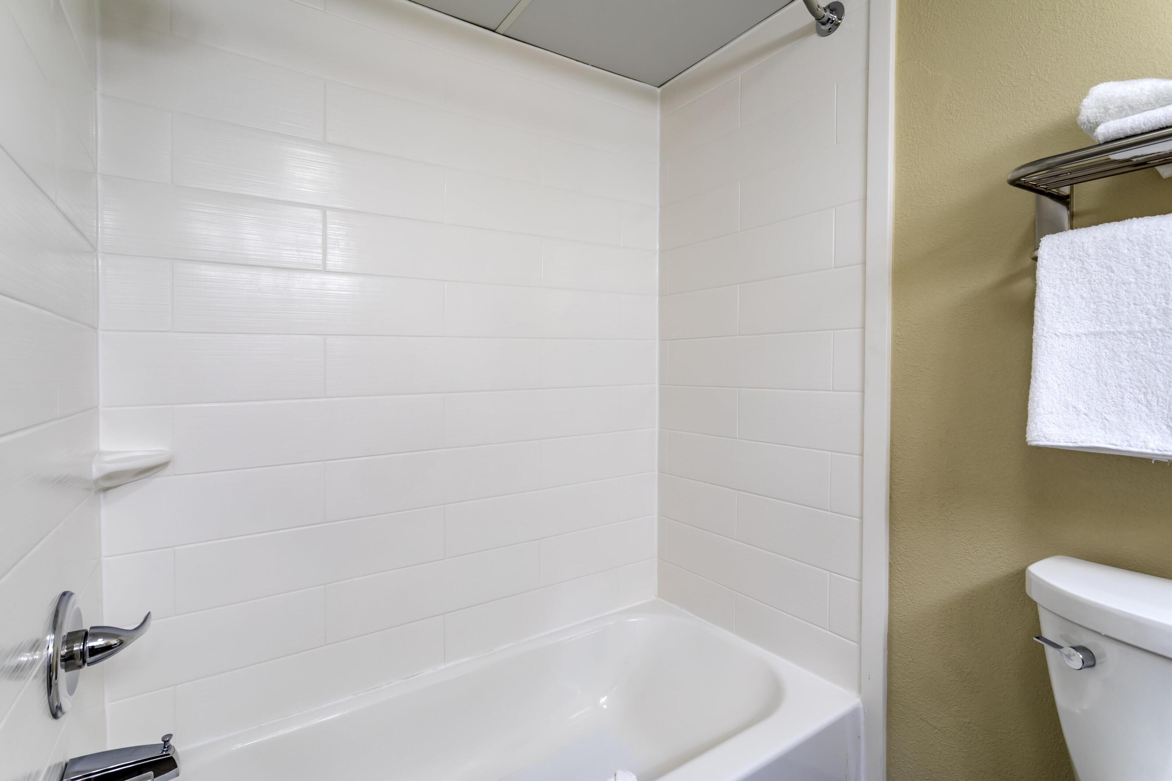 A bathroom with white tiled walls, a white bathtub, a toilet, and a towel rack with a towel.