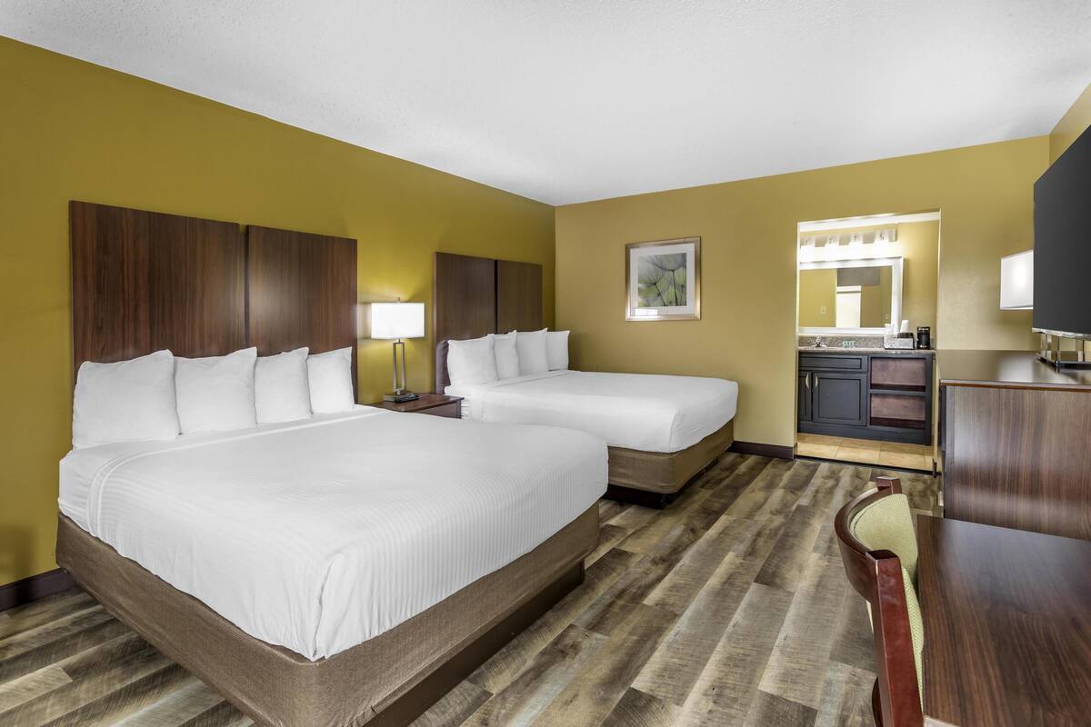 Une chambre d’hôtel avec deux lits, un bureau, une chaise, un miroir et une kitchenette.