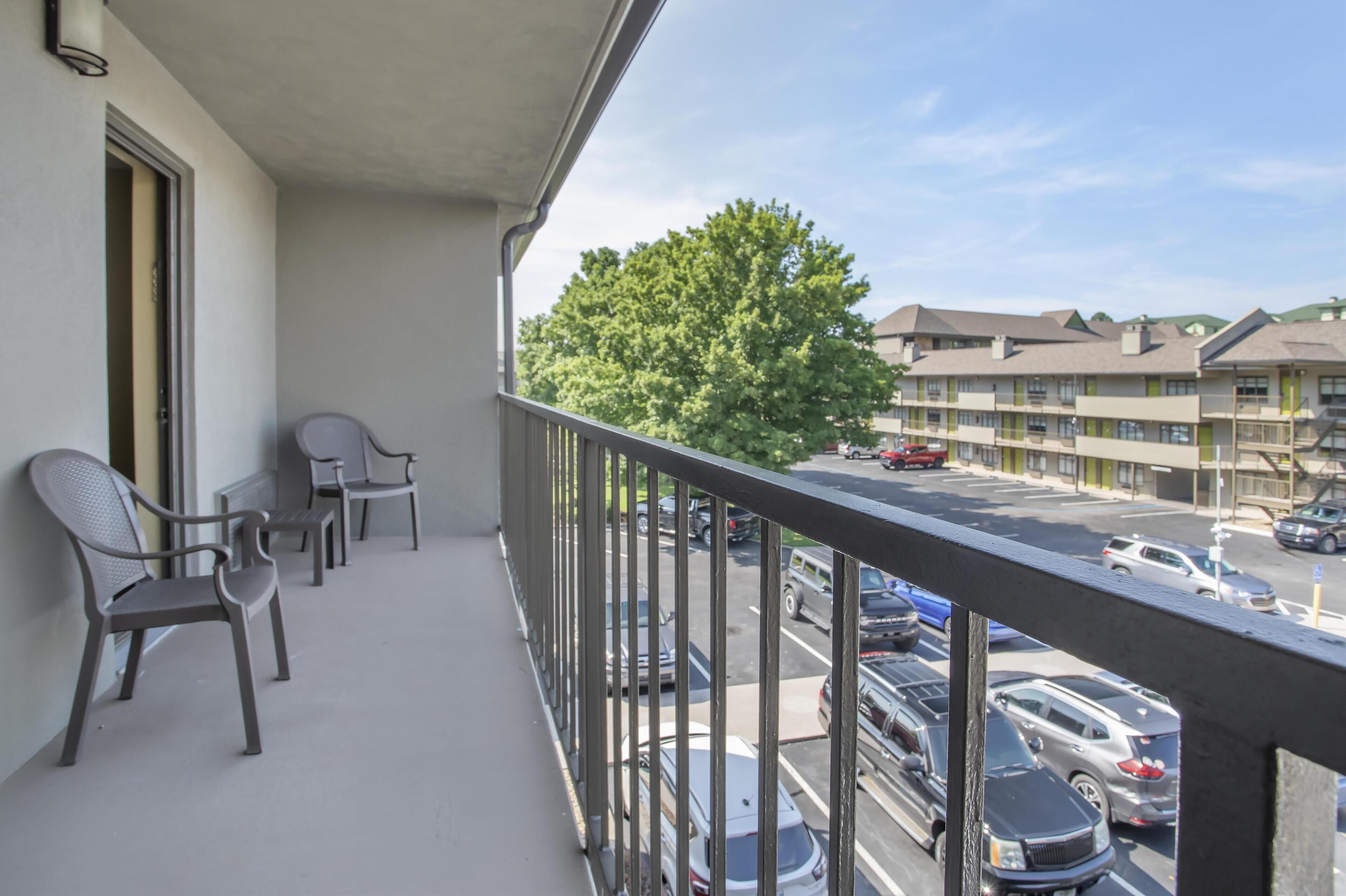 A balcony with chairs, a view of a parking lot, and buildings in the background.