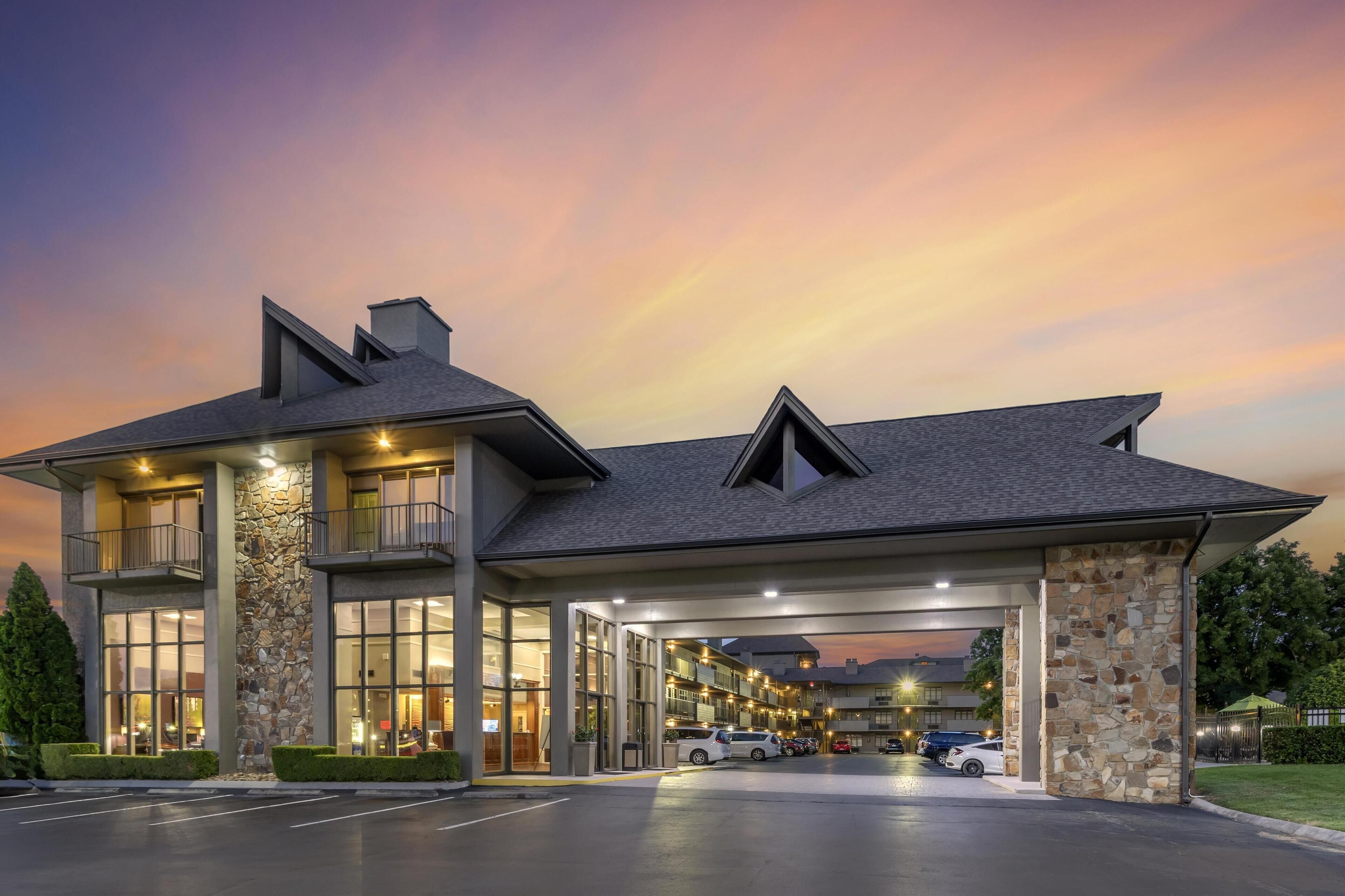 A modern hotel with a stone facade, large windows, and a covered parking area.