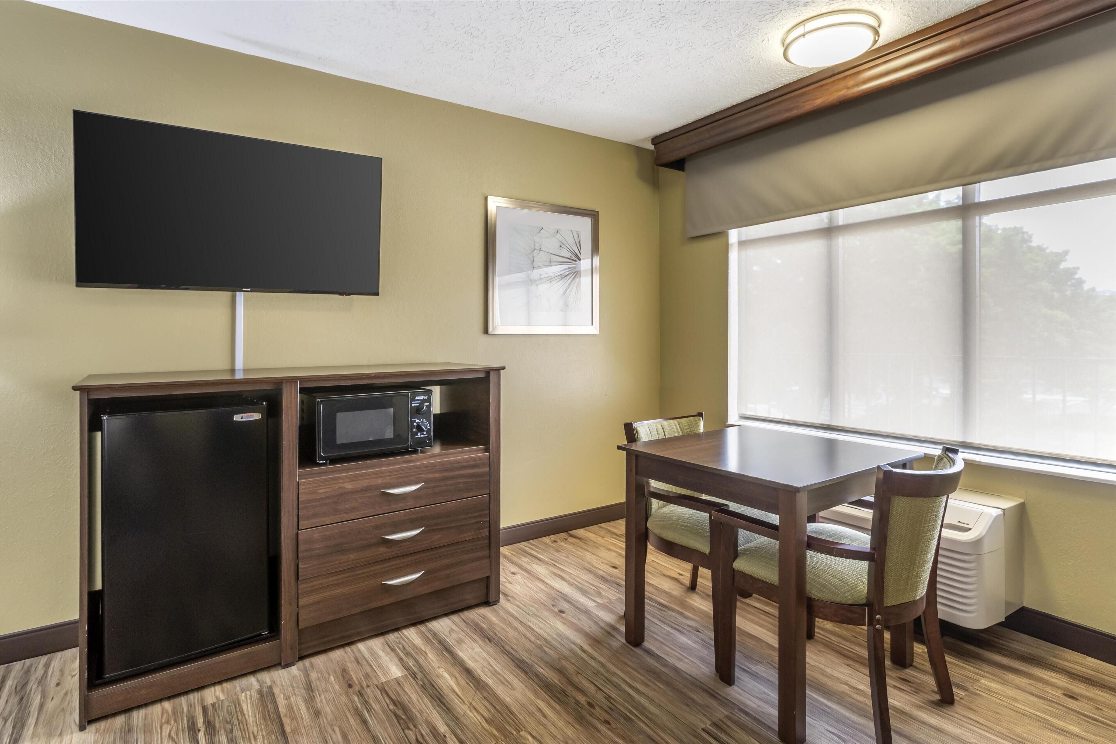 Una kitchenette compacta con microondas, un refrigerador pequeño y un televisor de pantalla plana montado en la pared.