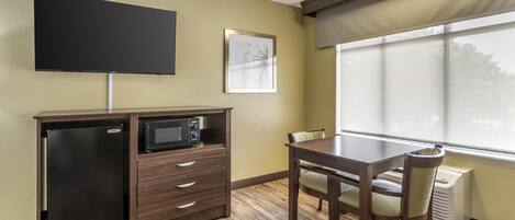 A compact kitchenette with a microwave, a small refrigerator, and a flat-screen TV mounted on the wall.