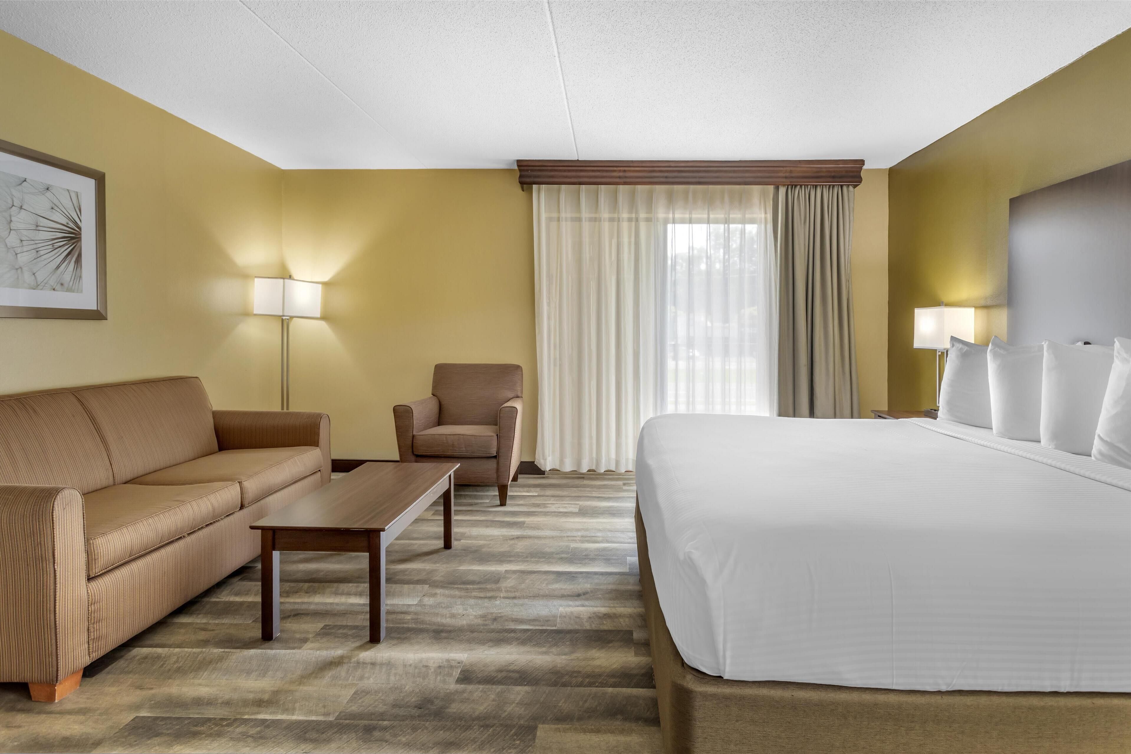 A hotel room with a bed, a sofa, a chair, a small table, and a lamp.
