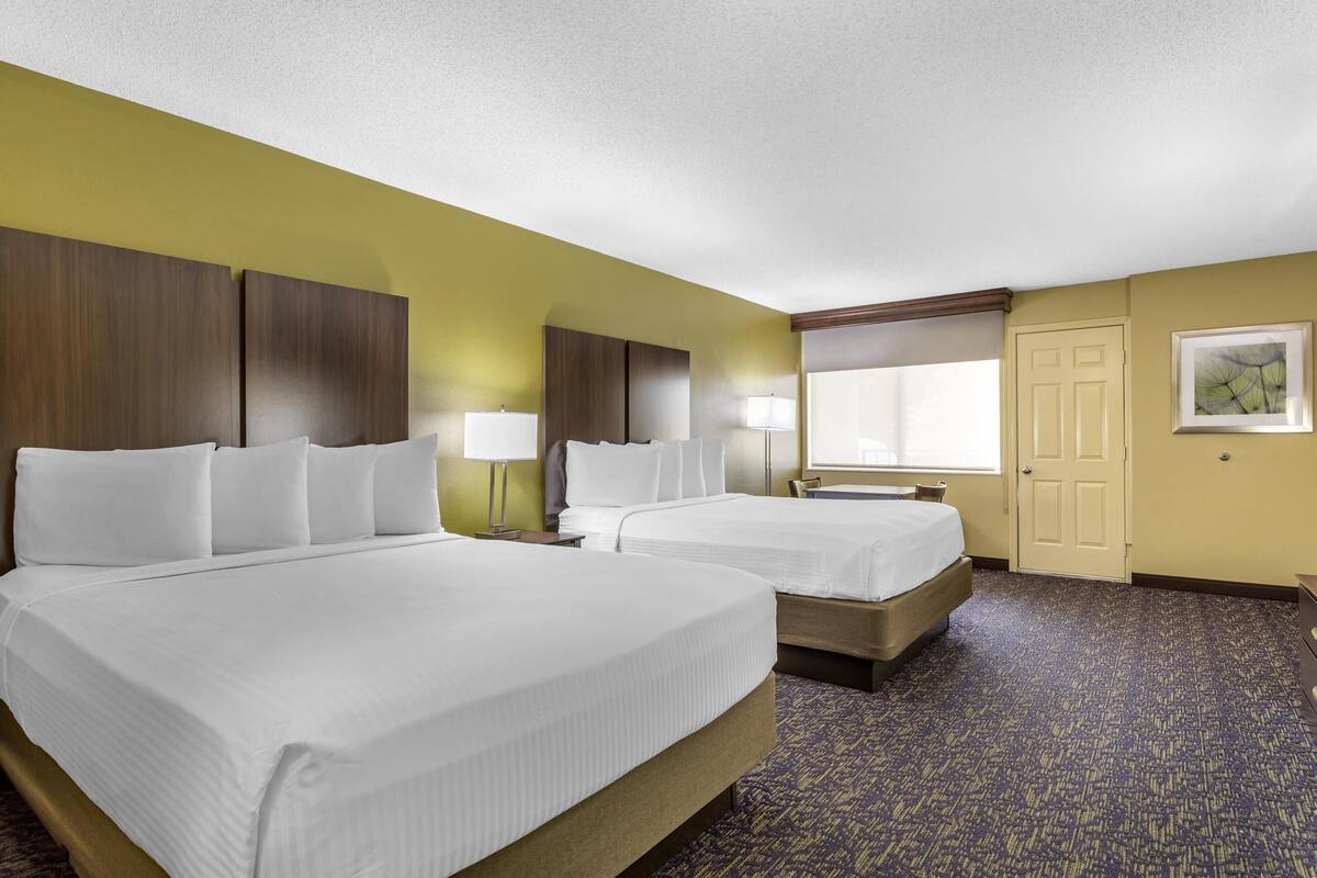 Une chambre d’hôtel avec deux lits, une fenêtre, une porte et une lampe.