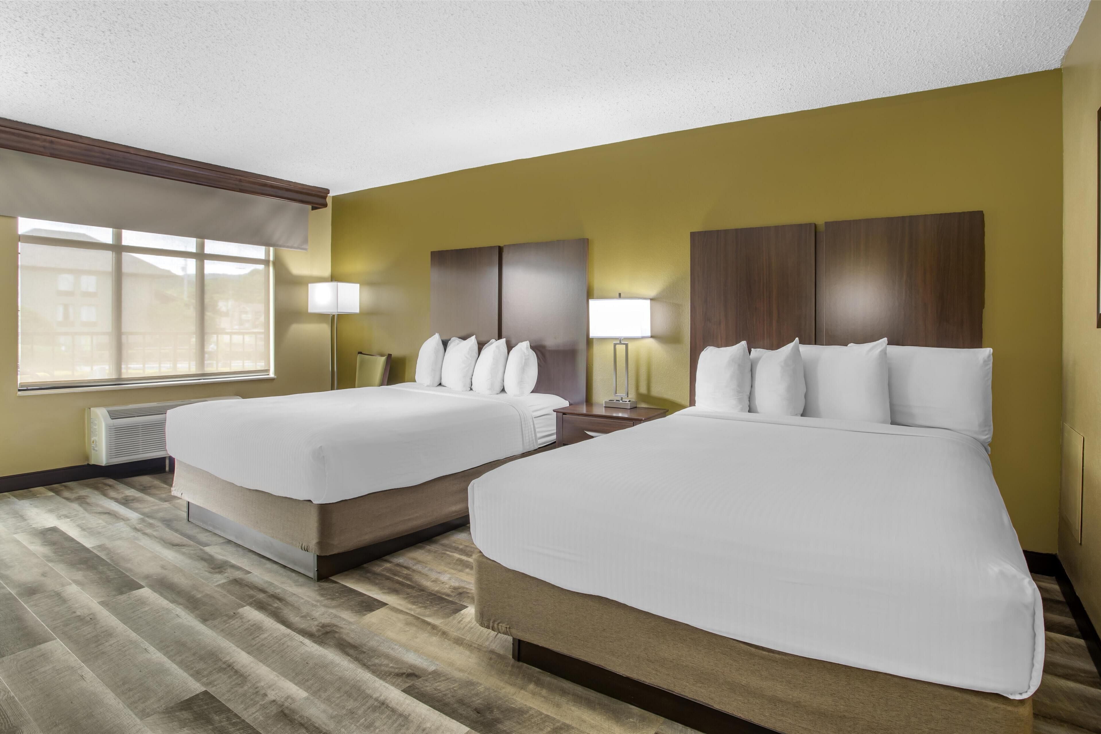 A hotel room with two beds, a large window, and a view of buildings outside.