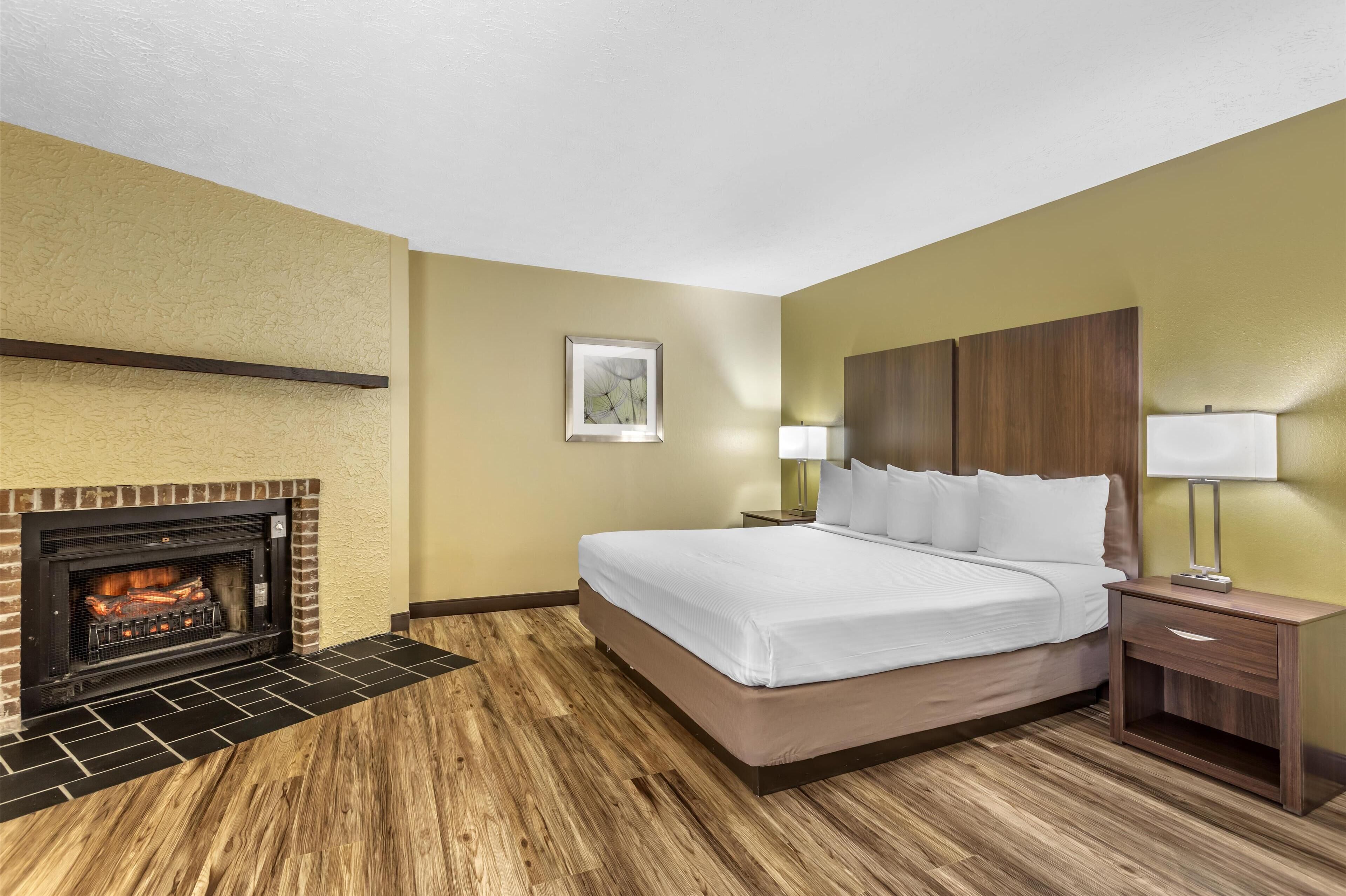 A hotel room with a bed, a nightstand, a lamp, a fireplace, and a framed picture on the wall.