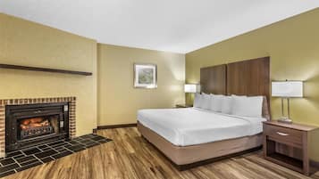 A hotel room with a bed, a nightstand, a lamp, a fireplace, and a framed picture on the wall.
