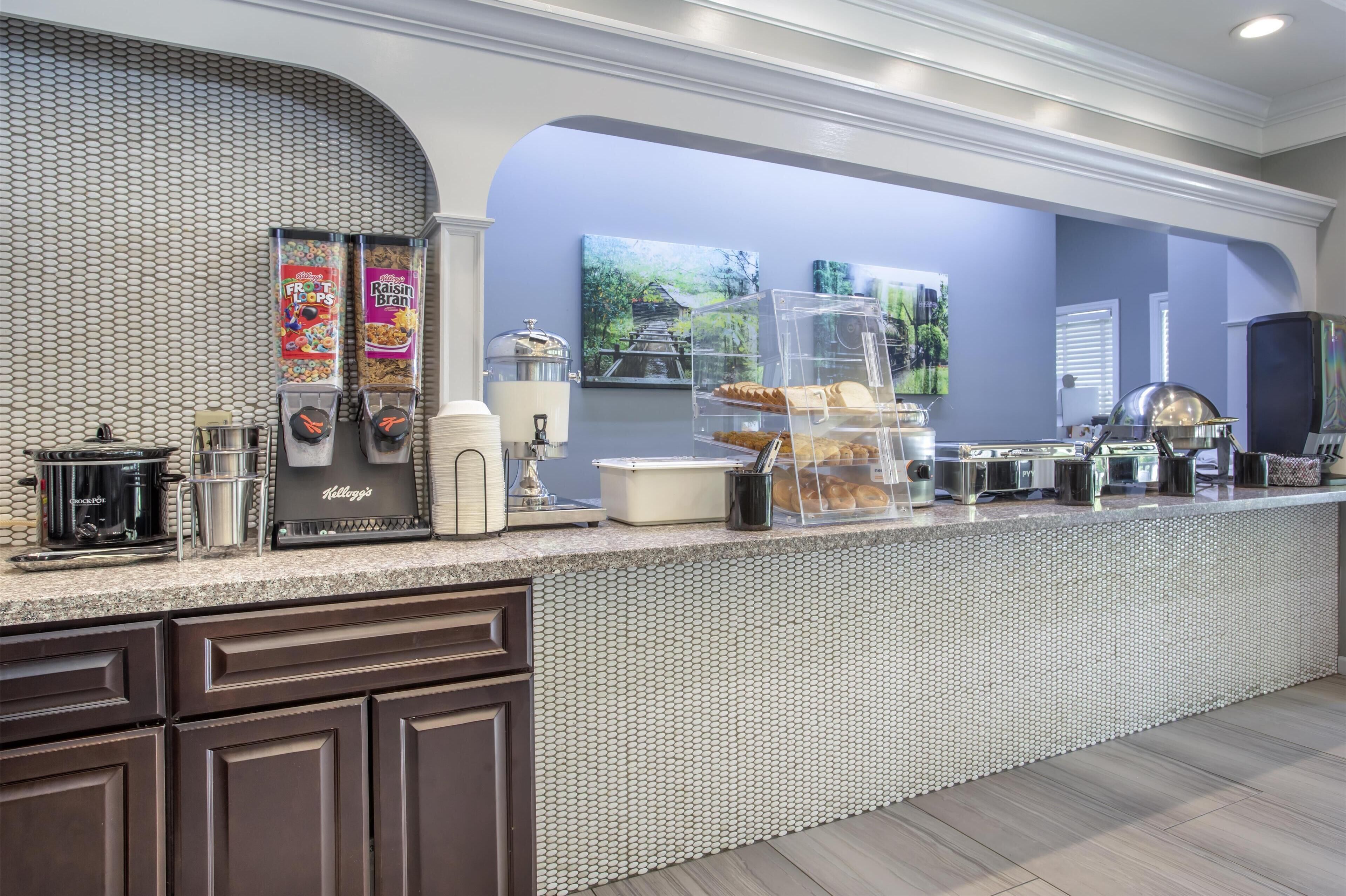 A breakfast bar with cereal dispensers, a coffee maker, and a fruit display.