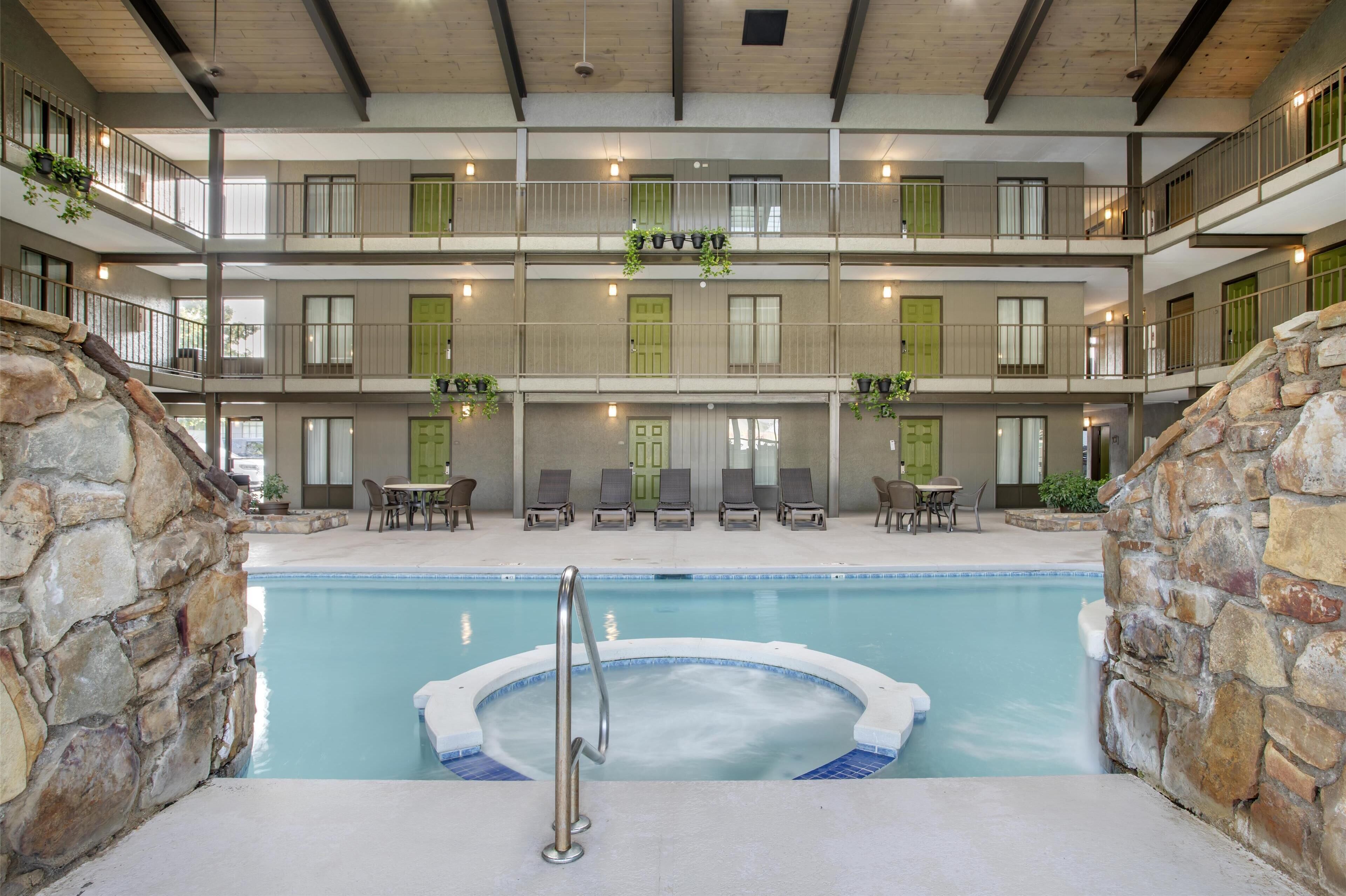 Une piscine intérieure à plusieurs niveaux, dotée d’un jacuzzi, de murs en pierre et de nombreux balcons avec des garde-corps.