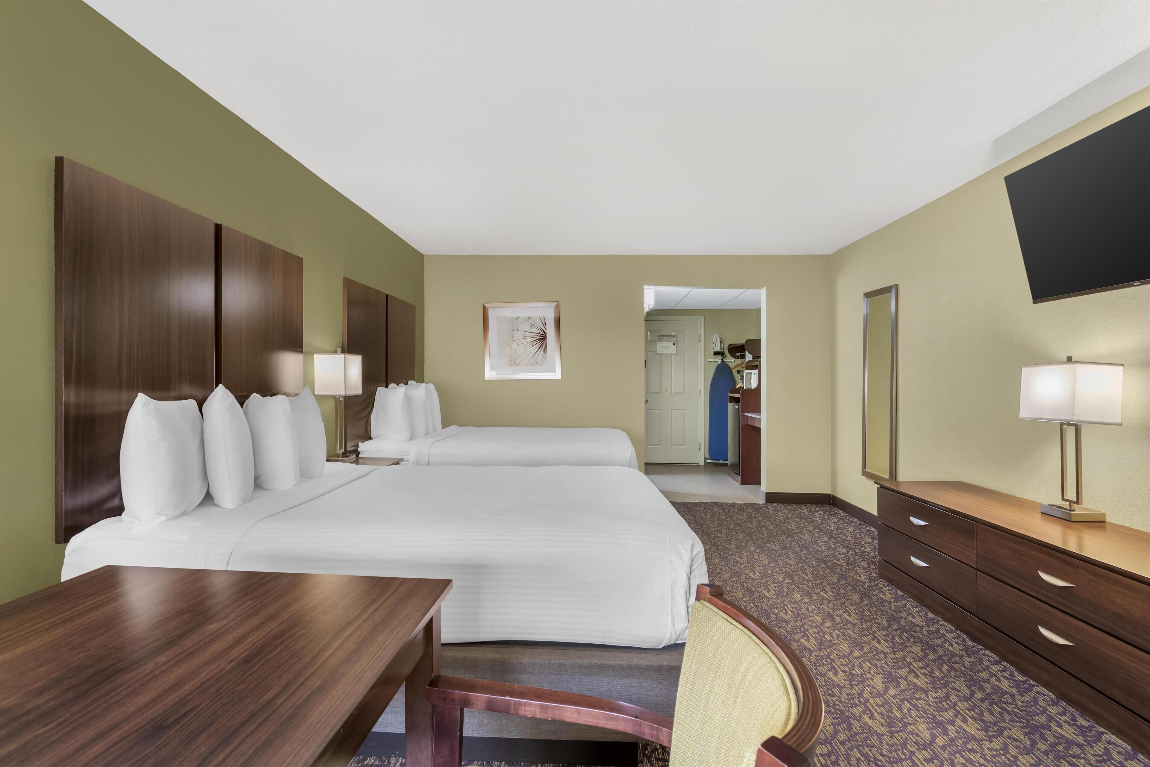 Une chambre d’hôtel avec deux lits, un bureau, une chaise, une commode et un téléviseur fixé au mur.