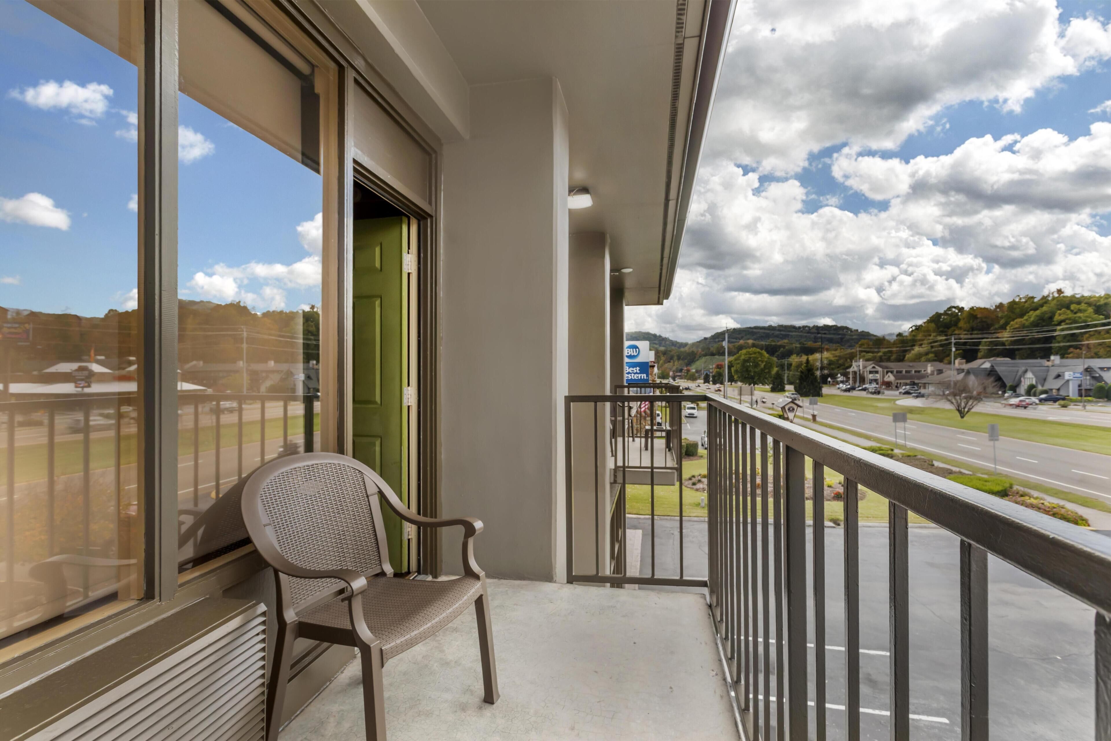 A balcony with a chair, a view of a road, and a sign for a parking area.