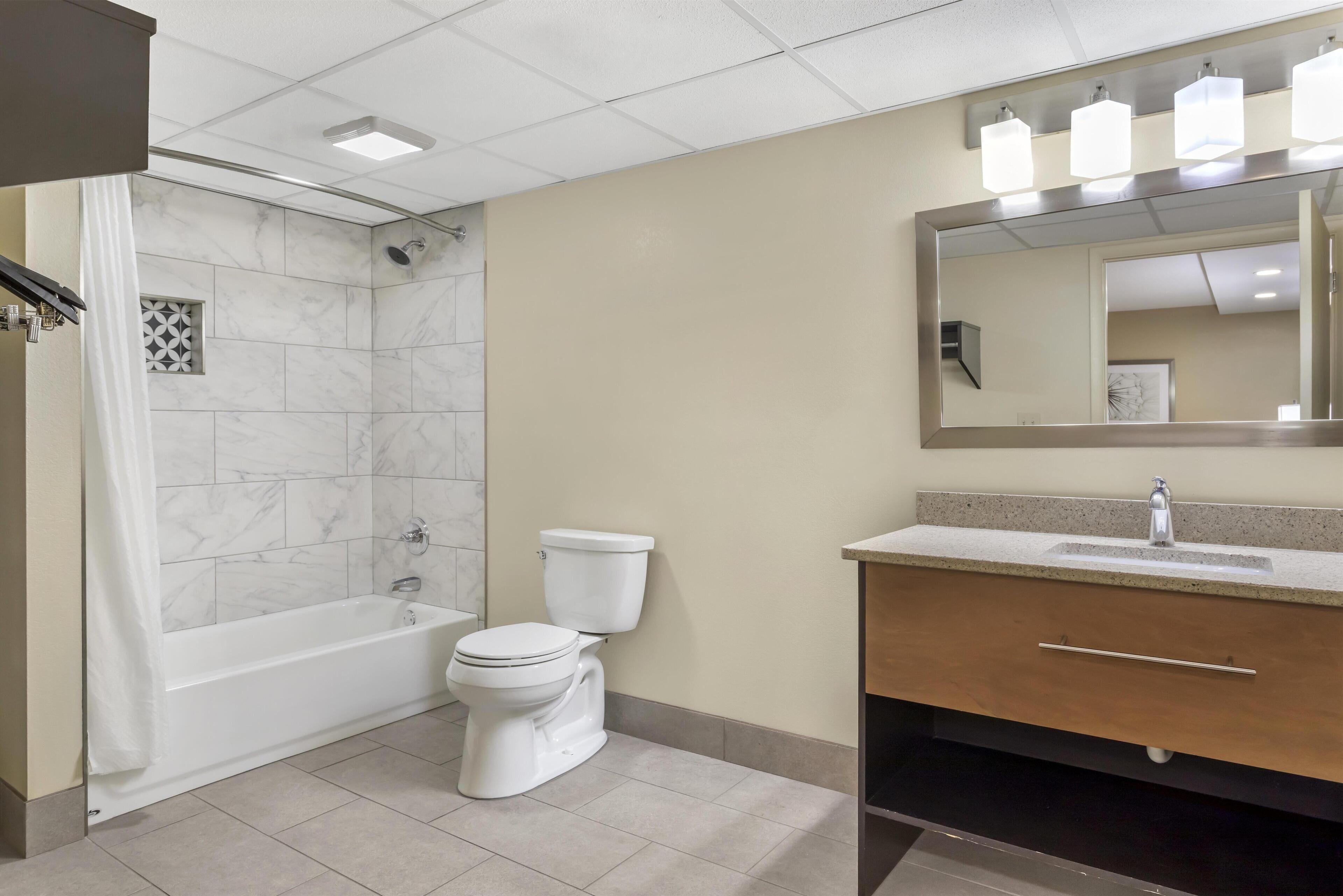 Et badeværelse med badekar, toilet og et vaskeskab med spejl.
