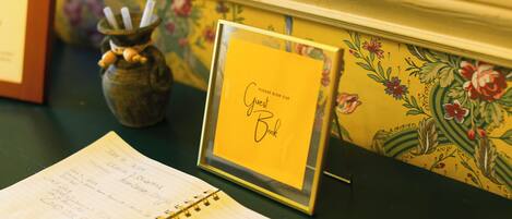 A notebook with handwritten notes, a framed sign requesting guests to sign a book, and a decorative vase.