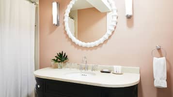 A bathroom with a white sink, black vanity, a round mirror, a towel rack, and a potted plant.