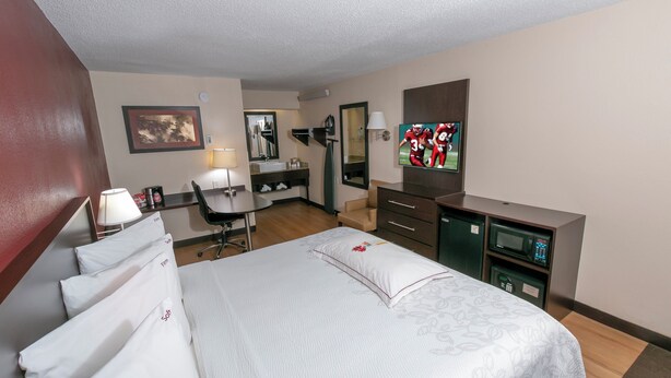 Ein Hotelzimmer mit Bett, Schreibtisch, Stuhl, Fernseher und Spiegel.