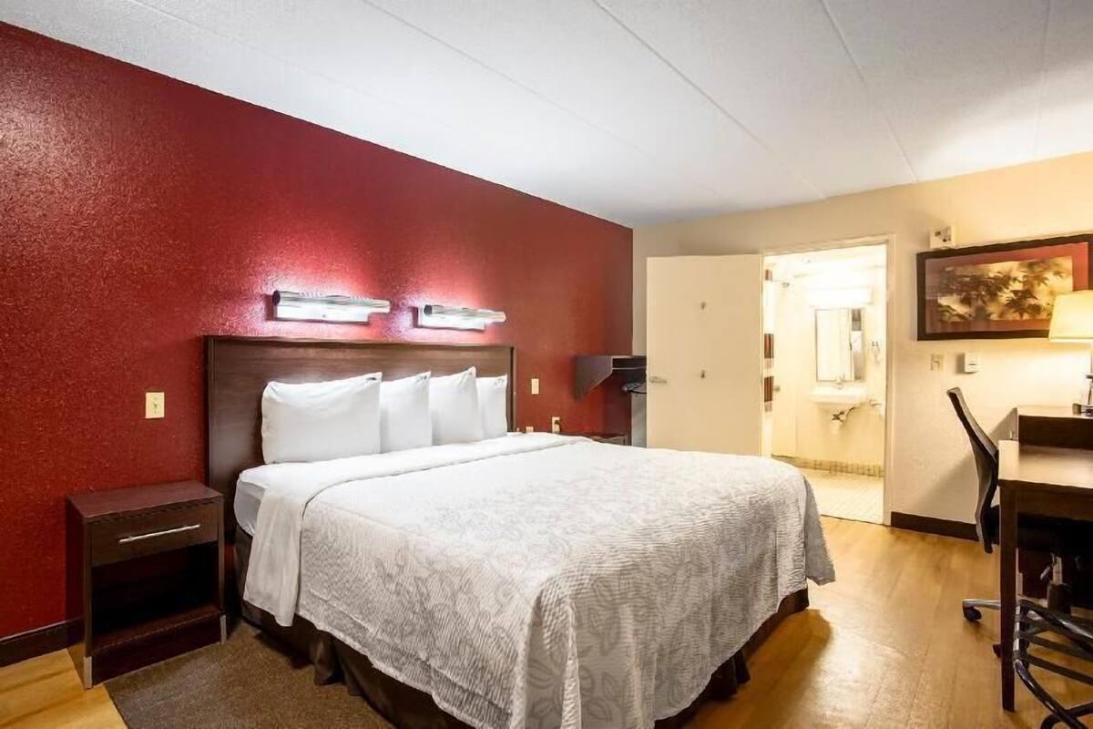 Ein Hotelzimmer mit Bett, Nachttisch, Schreibtisch, Stuhl und einer Tür zum Badezimmer.