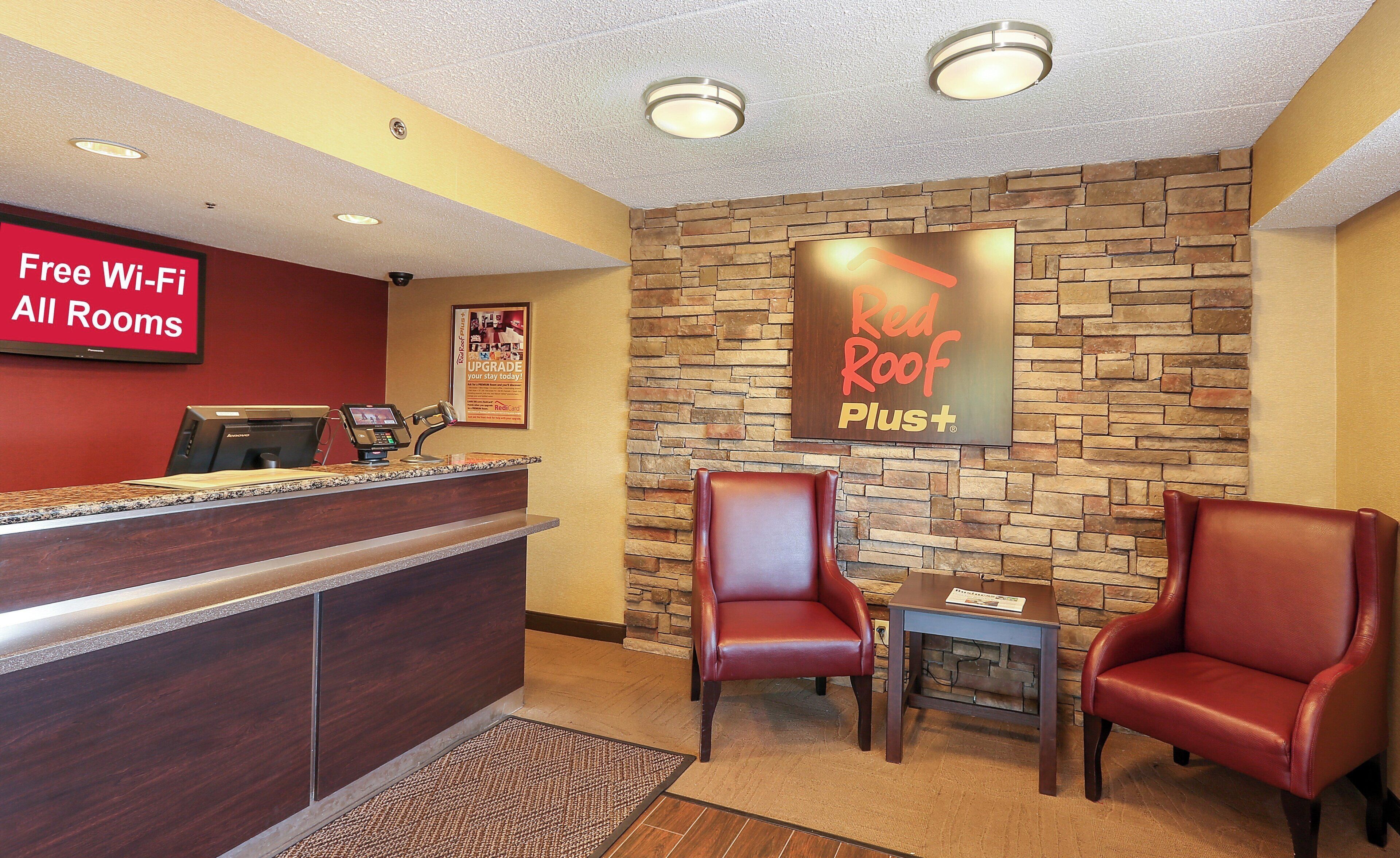 A reception area with a counter, a sign for free Wi-Fi, a Red Roof Plus sign, and two leather chairs.