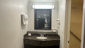 A bathroom with a granite countertop sink, a mirror, a towel rack, a hairdryer, and a trash can.