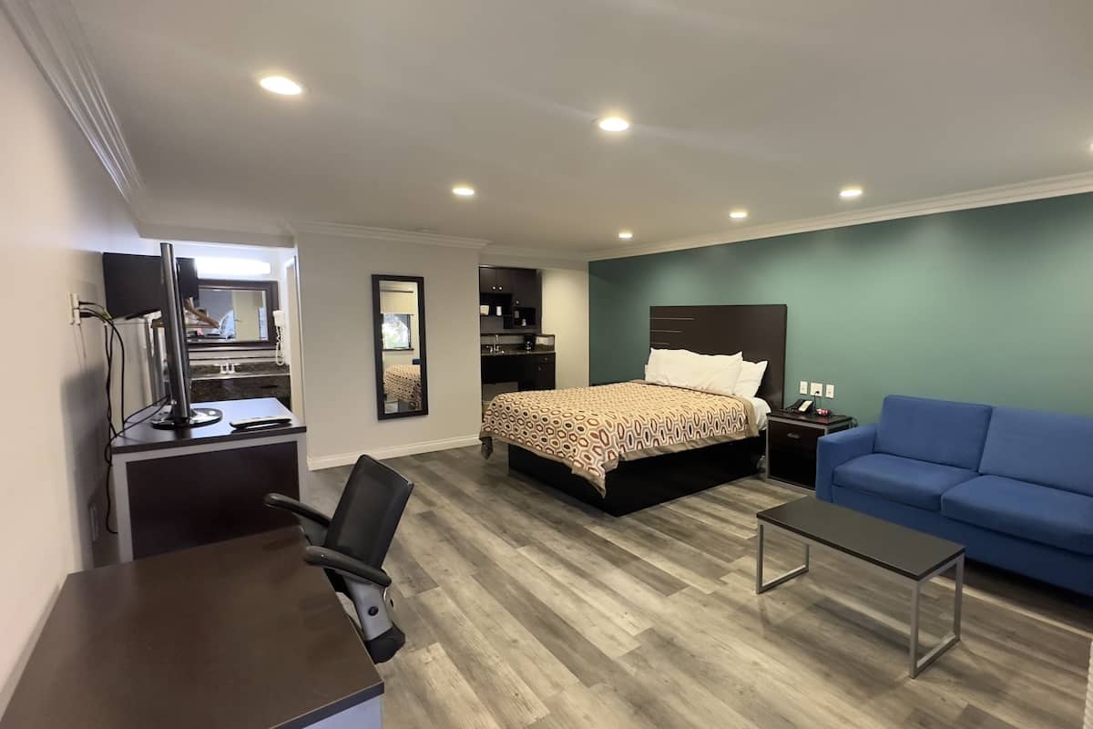 A hotel room with a bed, a desk, a chair, a blue sofa, and a small table.