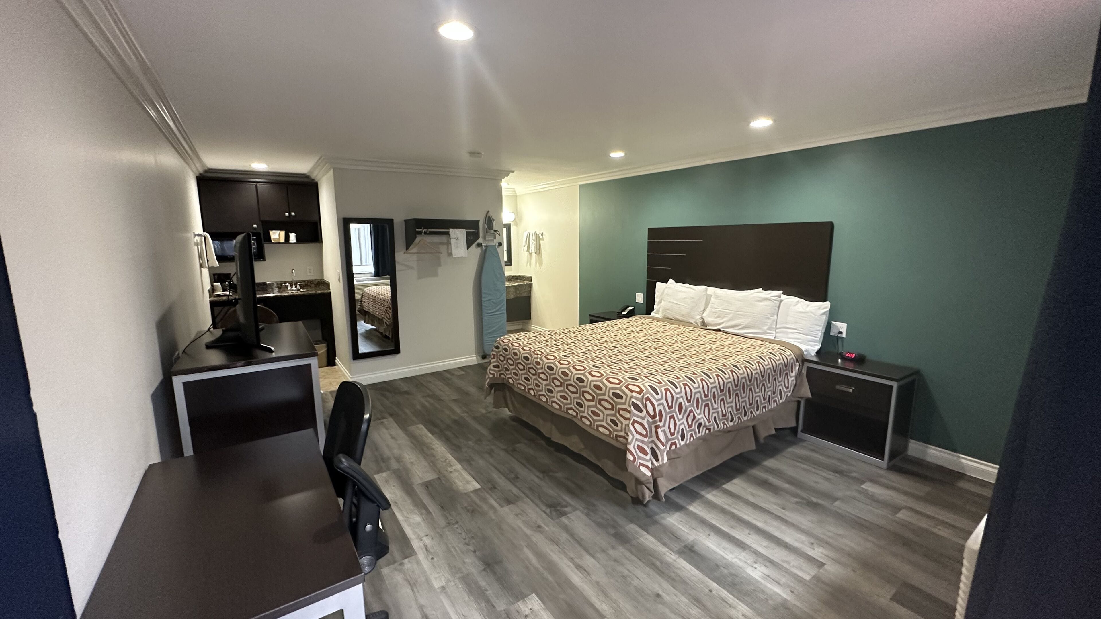 Quarto de hotel com cama, escrivaninha, cadeira, mesa pequena, espelho e mesa de cabeceira.