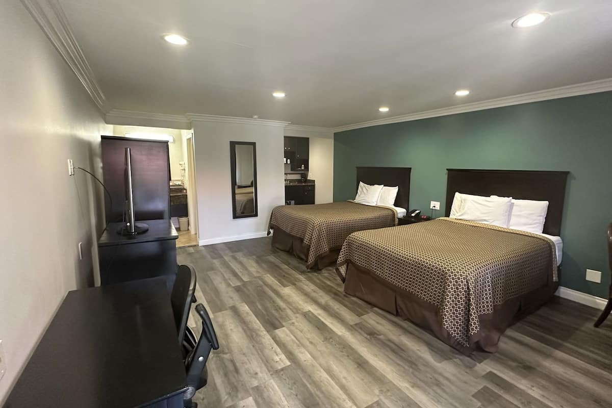 A hotel room with two beds, a desk, a chair, and a TV.