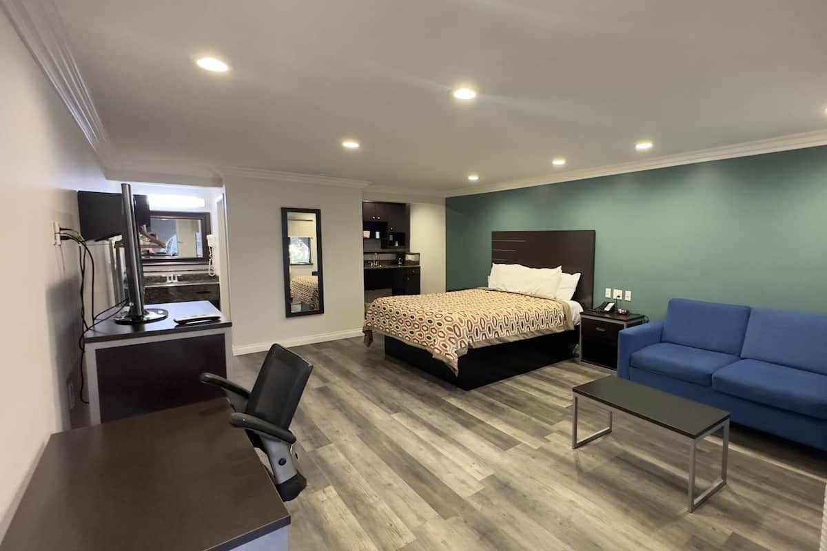 A hotel room with a bed, a desk, a chair, a blue couch, and a TV.