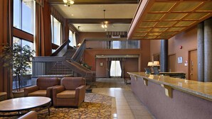 A lobby with a reception desk, seating area, staircase, and large windows.