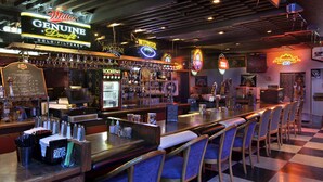 A bar area with a checkered floor, bar stools, and a neon sign for Miller Genuine Draft beer.