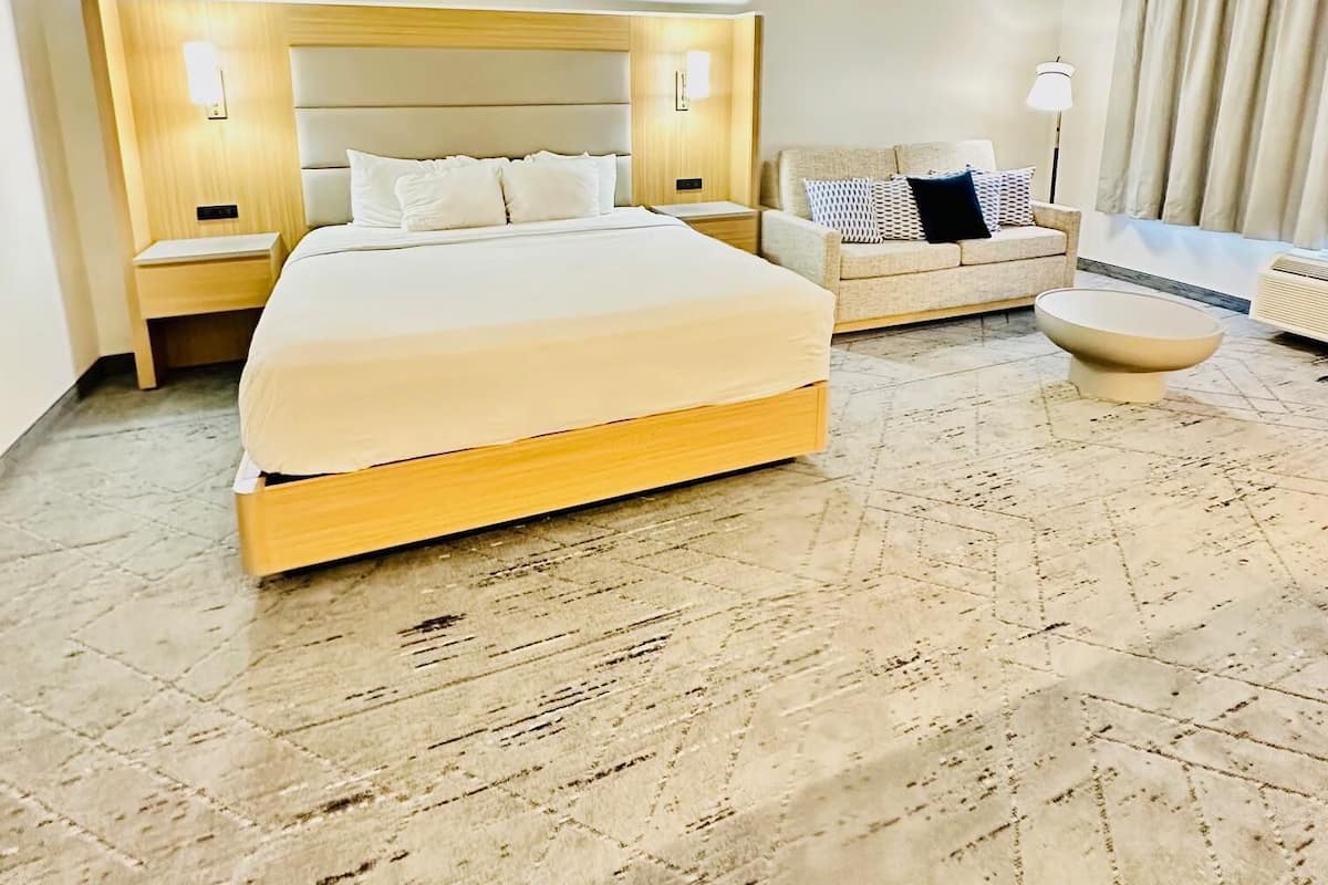 A hotel room with a large bed, a sofa, a small table, and a floor lamp.