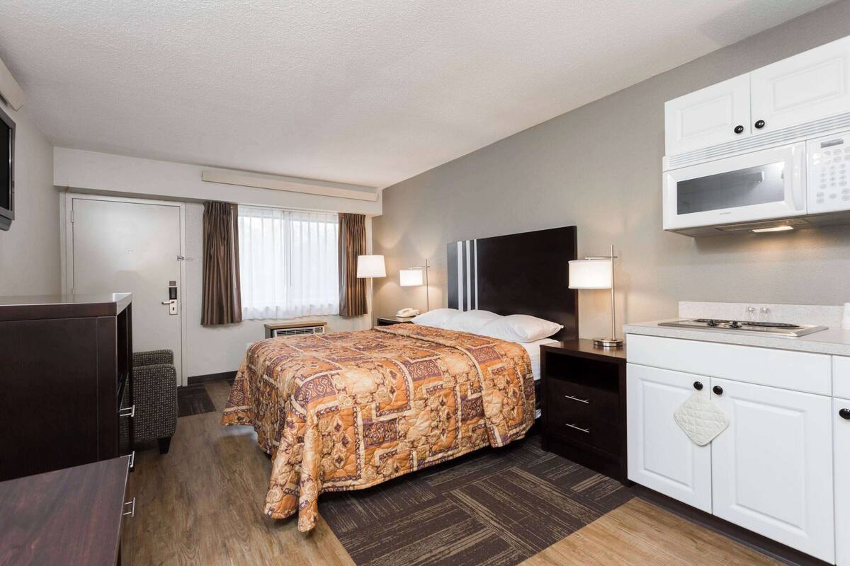 A hotel room with a bed, bedside tables, a TV, a microwave, and a kitchenette.
