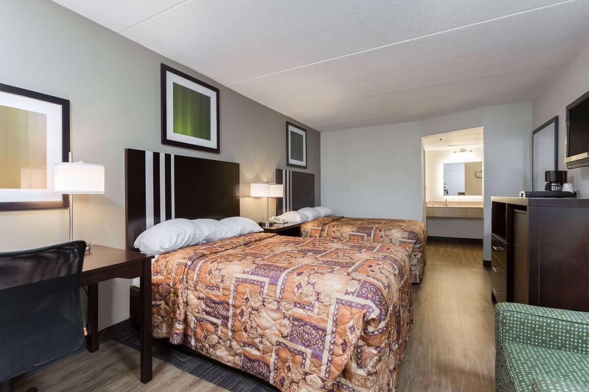 A hotel room with two beds, a desk, a chair, a dresser, and a mirror.