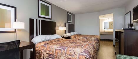 A hotel room with two beds, a desk, a chair, a dresser, and a mirror.