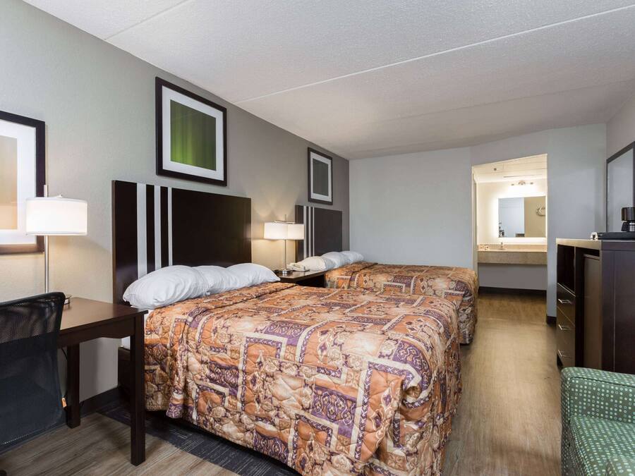 Quarto de hotel com duas camas, uma escrivaninha, uma cadeira, um armário e um espelho.