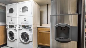 A laundry room with stacked washers and dryers, a stainless steel refrigerator, and wooden cabinets. - Days Inn by Wyndham Harrisburg North (Harrisburg)