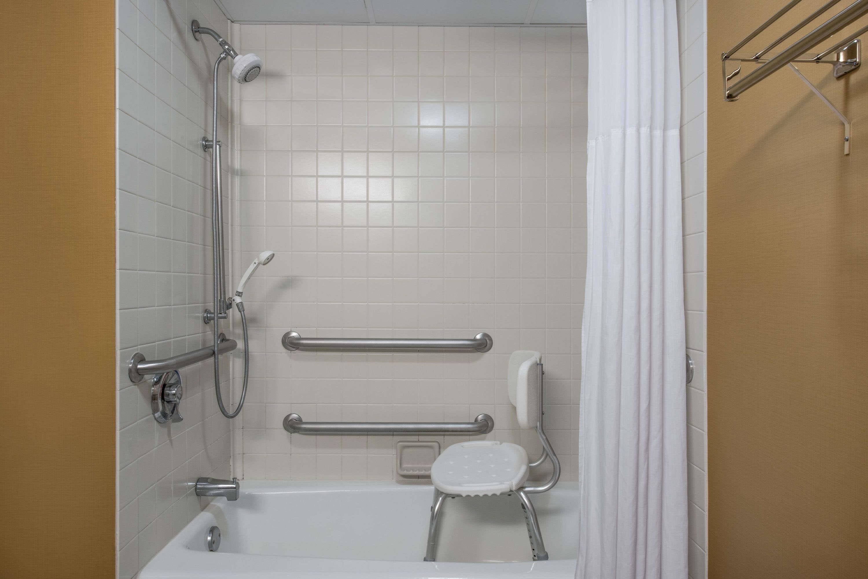 A bathroom with a white bathtub, grab bars, a showerhead, and a white shower curtain.