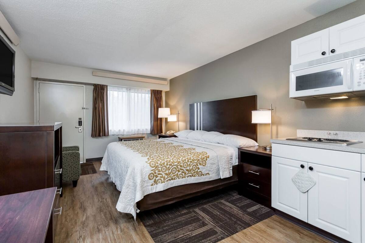 A hotel room with a bed, bedside table, lamp, microwave, and a small kitchenette.