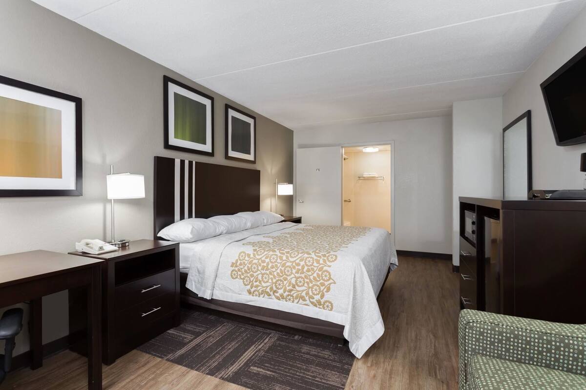 A hotel room with a bed, desk, chair, and a television.