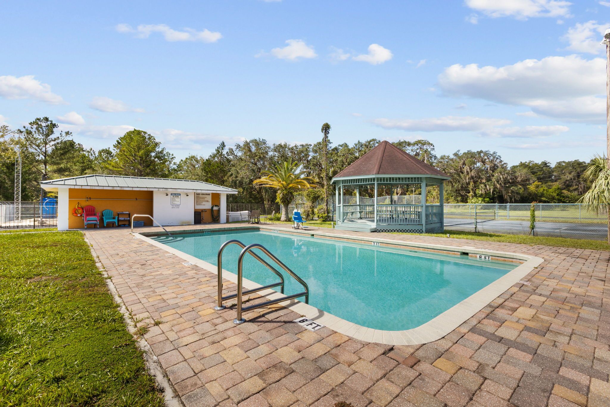 A swimming pool with a lifeguard station, a gazebo, and a covered seating area with chairs.